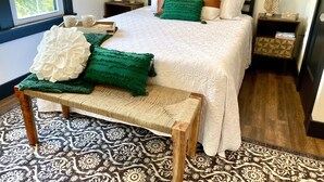 Une chambre à coucher bien aménagée, avec un grand lit, deux tables de chevet, un banc et un tapis à motifs.