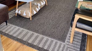 Un salon moderne avec un escalier, un téléviseur à écran plat, un canapé en cuir marron, une table basse blanche et un tapis à motifs.