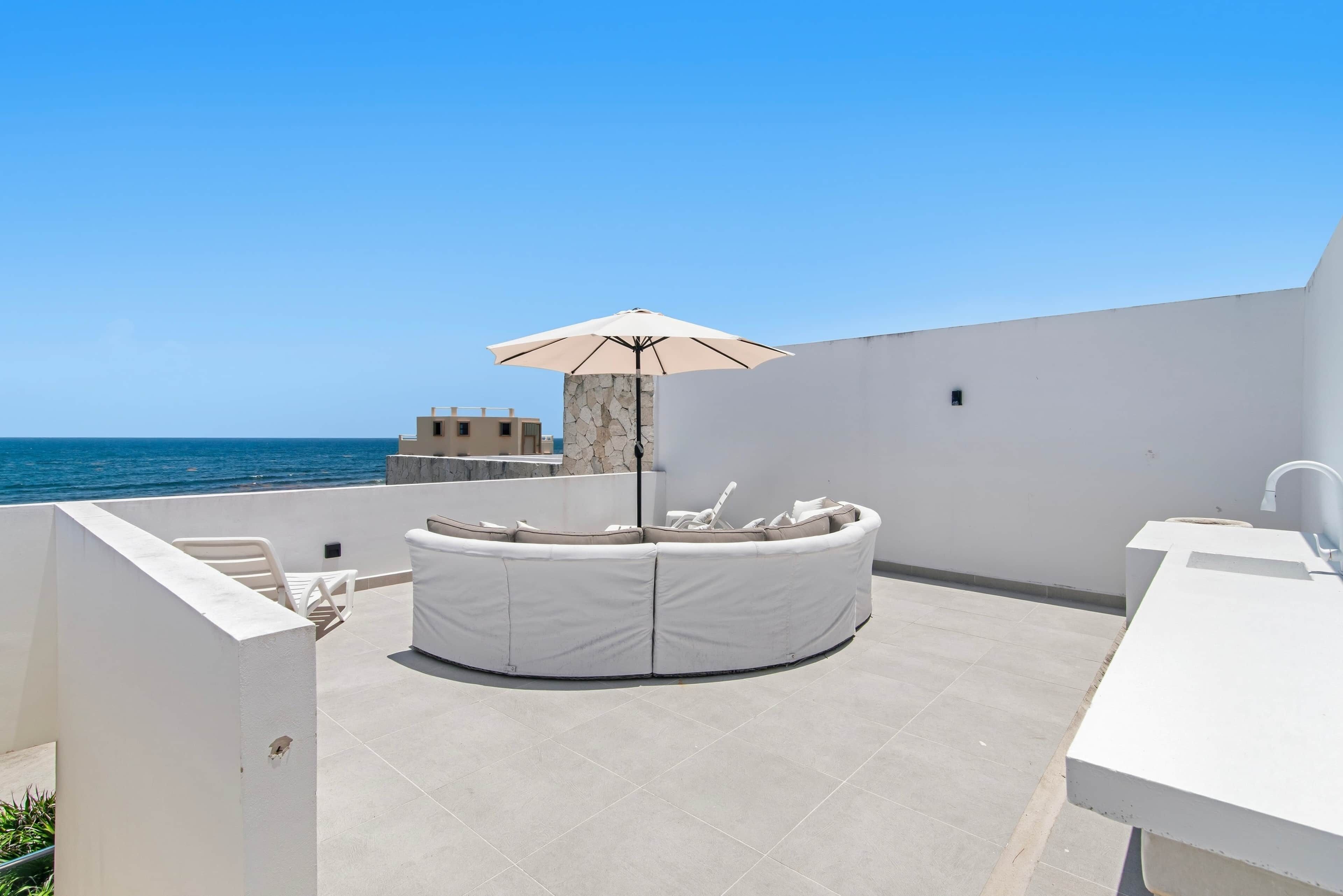 A rooftop terrace with a round seating area, a table, and a large umbrella.