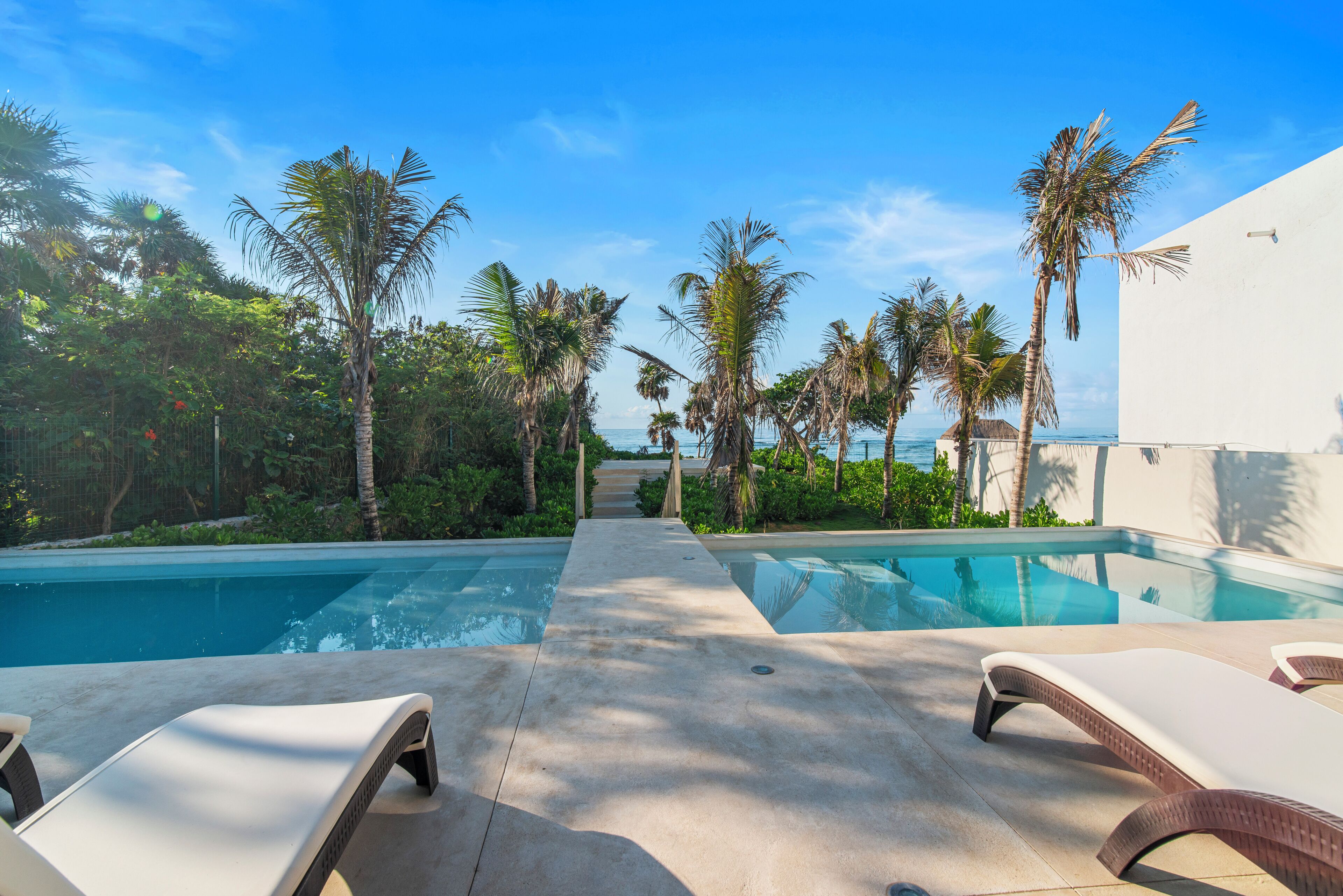 A pool area with lounge chairs, palm trees, and a clear view of the ocean.