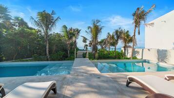 A pool area with lounge chairs, palm trees, and a clear view of the ocean.