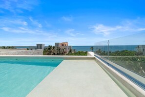 A rooftop pool with a clear view of the ocean and a modern building in the background.