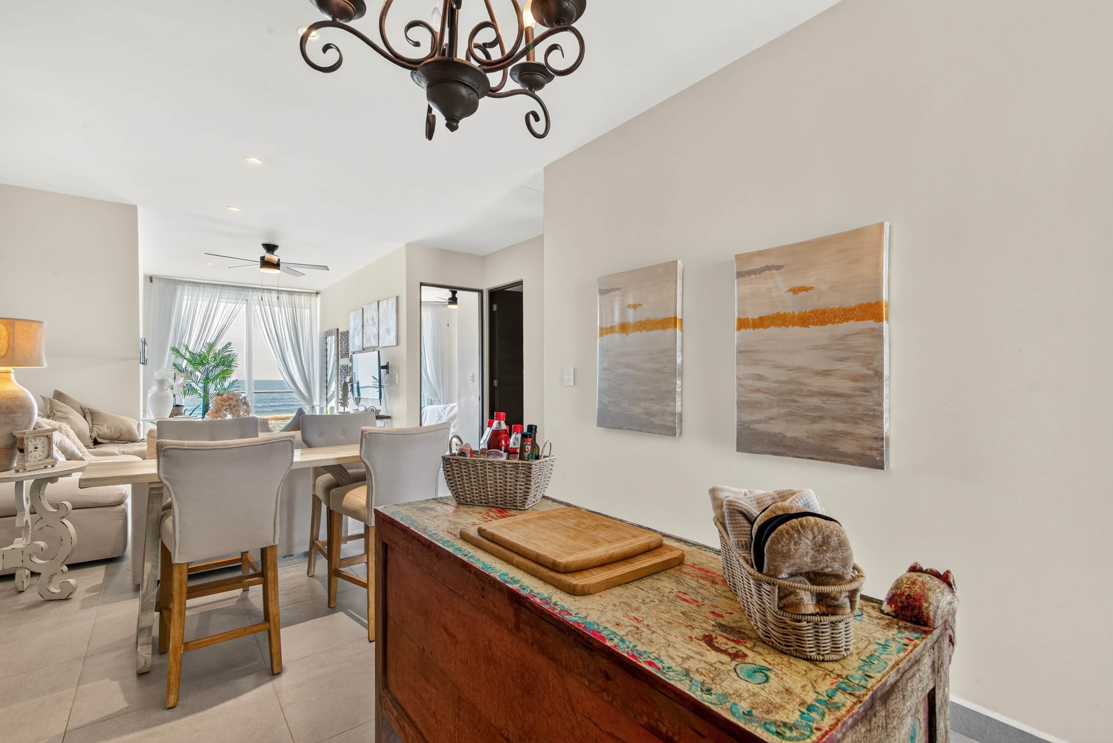 A modern kitchen with a wooden island, a dining area with chairs, and a view of the sea through the window.