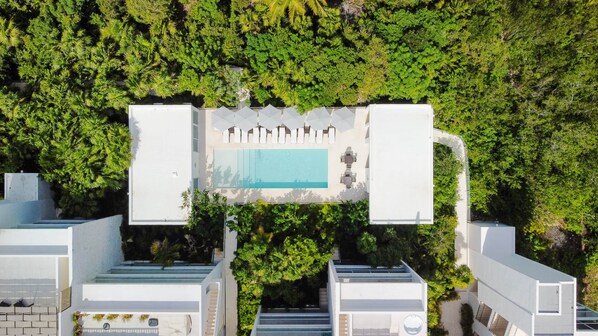 An aerial view of a modern building with a rooftop pool surrounded by lush greenery.