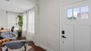 A modern living room with a white door, a large potted plant, a grey armchair, and a small table. - Med Center 2BR | Gated, Near NRG, MD Anderson (Houston)