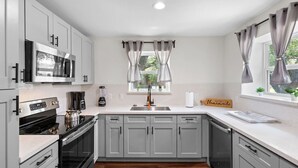 A modern kitchen with grey cabinets, a stainless steel microwave, a coffee maker, and a blender. - Med Center 2BR | Gated, Near NRG, MD Anderson (Houston)