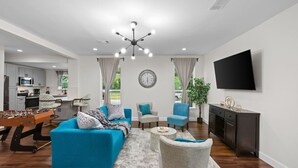 Un salon moderne avec un baby-foot, un canapé bleu, un fauteuil gris et un téléviseur fixé au mur.