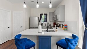 Une cuisine moderne avec un îlot central, des meubles blancs et des chaises bleues.