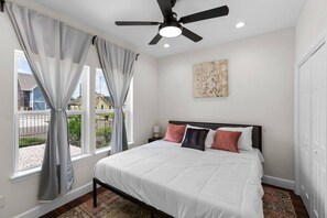 A bedroom with a bed, a ceiling fan, a window with curtains, a nightstand, and a painting on the wall. - Med Center 5BR Duplex | Gated, Near NRG, TMC (Houston)