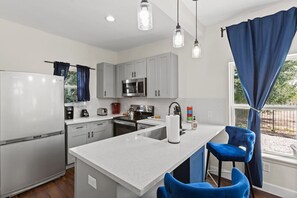 A modern kitchen with a central island, stainless steel appliances, and blue bar stools. - Med Center 5BR Duplex | Gated, Near NRG, TMC (Houston)
