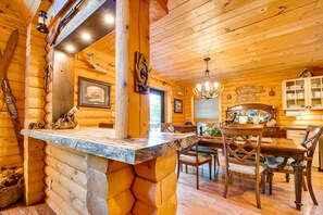 L’intérieur d’une cabane en rondins, avec une table à manger en bois, des chaises, un lustre et une cheminée.