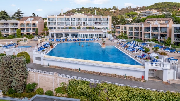 A large swimming pool surrounded by lounge chairs and umbrellas, with a building in the background. - Appartement Wemyssia - Welkeys (Cannes)