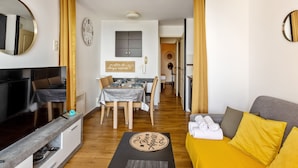 A modern living room with a TV, sofa, and a dining area with a table and chairs. - Appartement Wemyssia - Welkeys (Cannes)