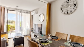 A dining area with a table set for four, a large wall clock, and a sliding glass door leading to a balcony. - Appartement Wemyssia - Welkeys (Cannes)