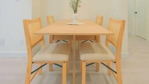 Een eettafel met vier stoelen, een vaas met bloemen en een effen muur op de achtergrond.