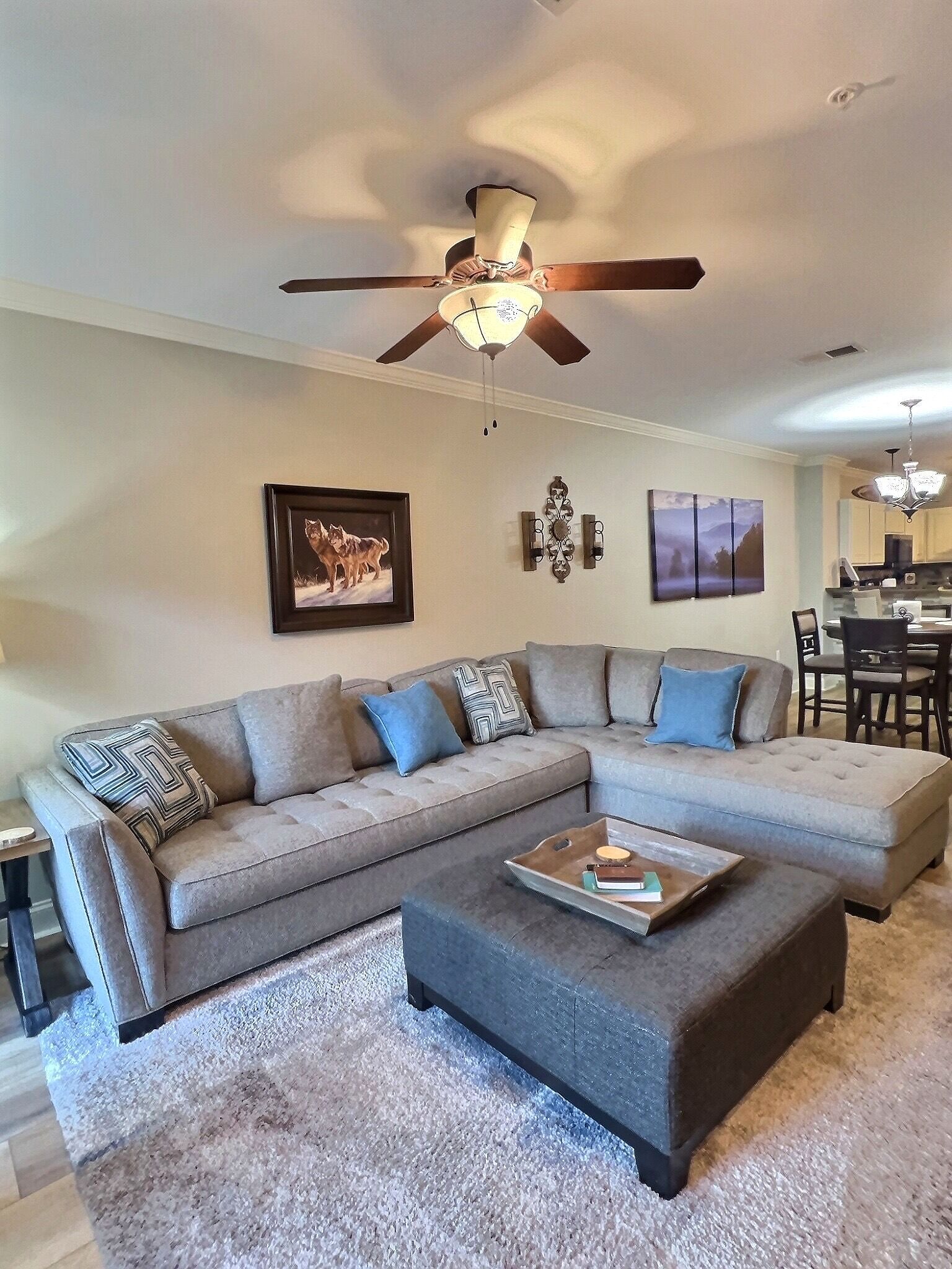 A living room with a sectional sofa, a coffee table, a ceiling fan, and artwork on the walls.
