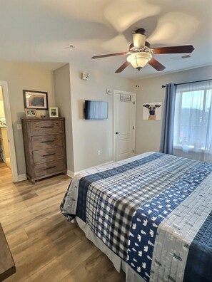 Un dormitorio con una cama, ventilador de techo, cómoda, televisor y una puerta.