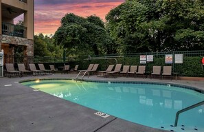 Una piscina con sillas de descanso, un muro de piedra y vistas a árboles.