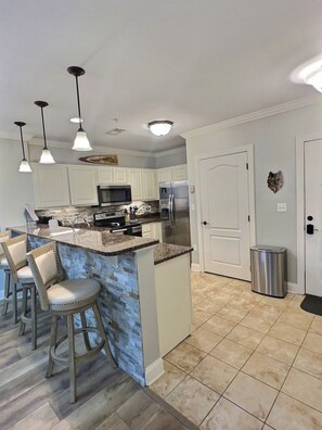 Una cocina moderna con una isla central, taburetes de bar, luces colgantes y un microondas.
