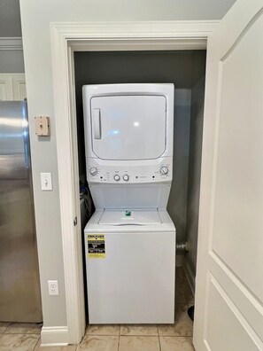 A compact washer and dryer unit in a small laundry room with a door leading to another room.