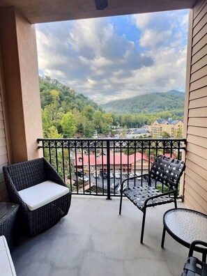 A balcony with wicker furniture, a glass table, and a view of a town and mountains.
