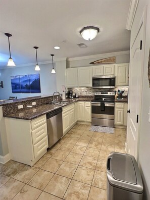 A modern kitchen with white cabinetry, a stainless steel dishwasher, a built-in oven, and a microwave.