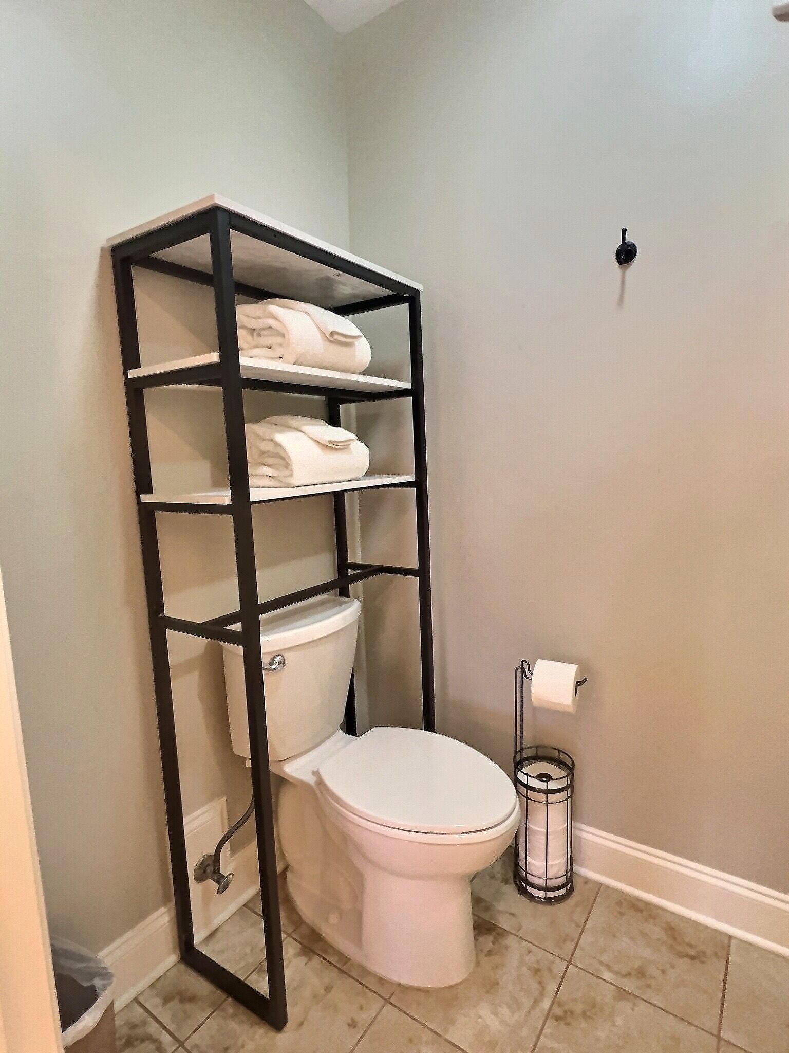 Un bagno con il water bianco, una scaffalatura in metallo nero con asciugamani e un portasciugamani.