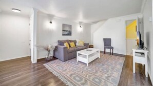 Een moderne woonkamer met een grijze bank, een witte salontafel, een vloerkleed met een patroon en een klein bijzettafeltje.