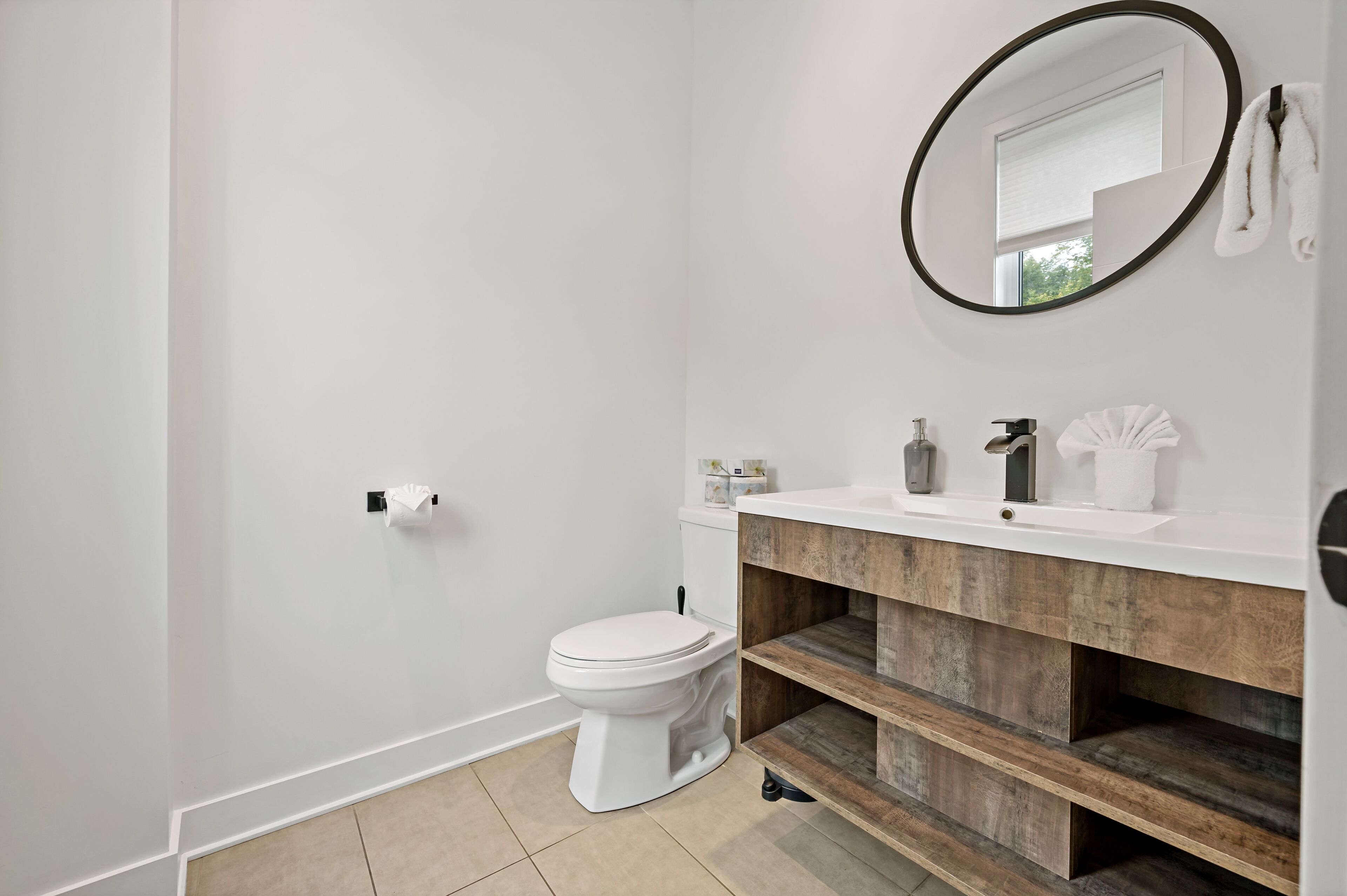 A modern bathroom with a white toilet, wooden vanity, and a round mirror.