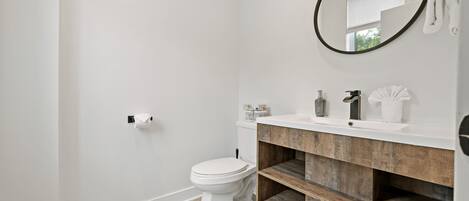 A modern bathroom with a white toilet, wooden vanity, and a round mirror.
