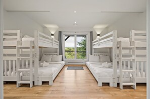A room with two bunk beds, a large window with a view of greenery, and a wooden floor.
