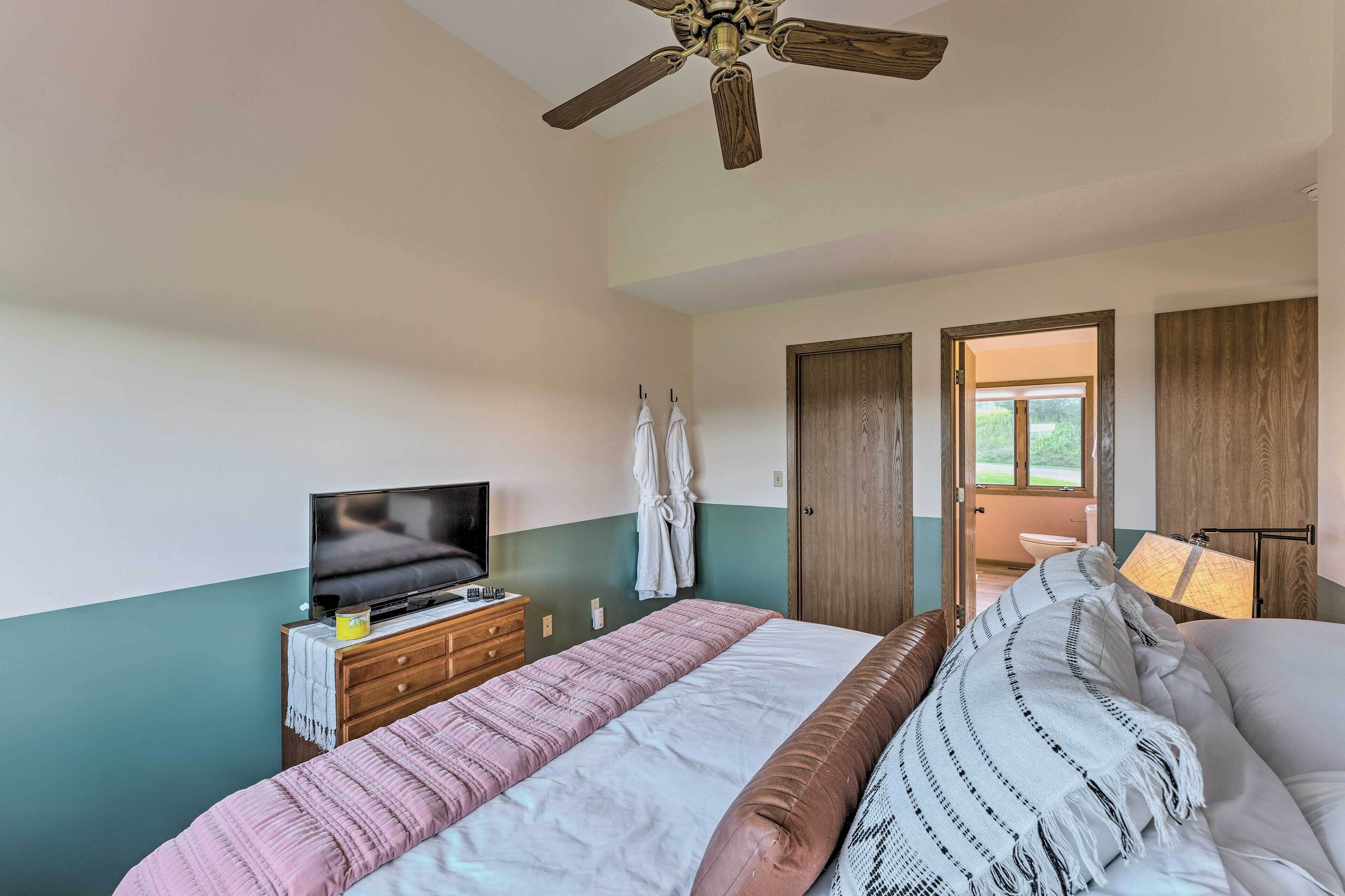 A bedroom with a bed, a TV, a ceiling fan, and a view of the outdoors.