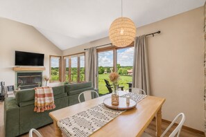 A modern living room with a green sofa, a wooden dining table, and a large window offering a view of a green landscape. - Boutique townhome w/ fire pit, KING bed, mezzanine loft & golf views! (Galena)