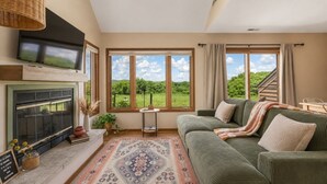 Un salon chaleureux avec une cheminée, de grandes fenêtres, un canapé vert et un tapis à motifs.