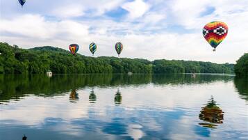A calm lake with hot air balloons in the distance and a boat on the water.