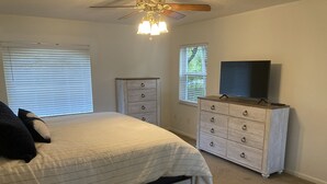 Een slaapkamer met een bed, een dressoir, een televisie en een plafondventilator.