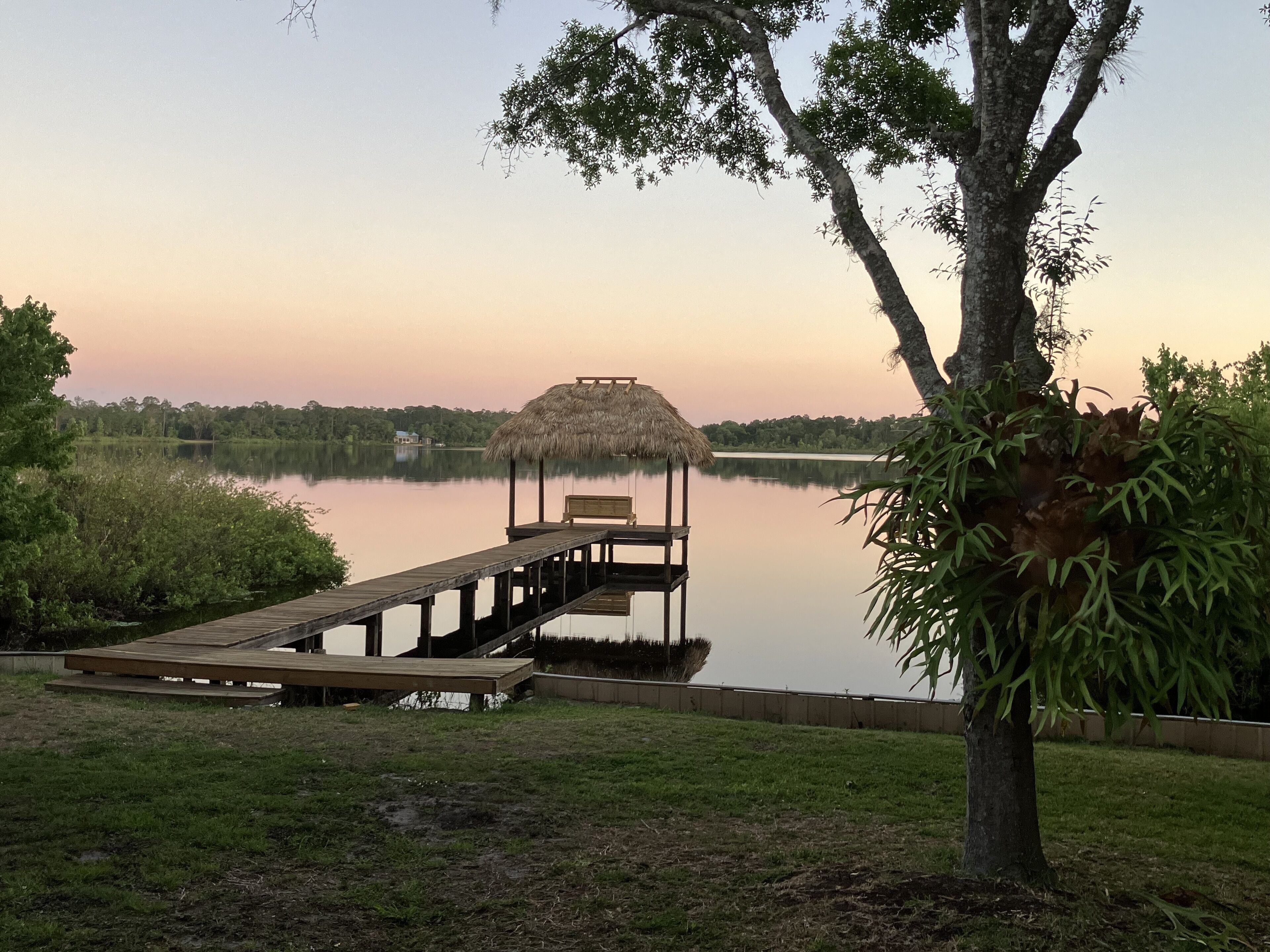 A wooden dock extending into a calm lake, with a thatched-roof gazebo at the end.