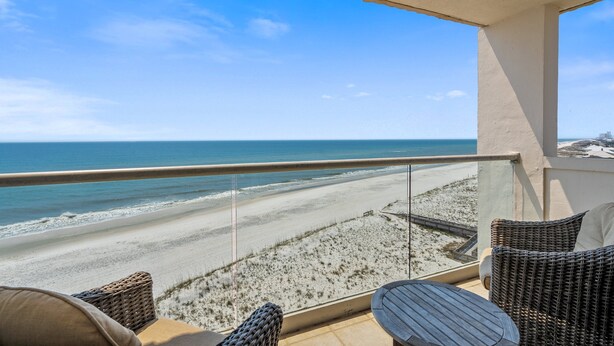 A balcony with wicker furniture overlooking a beach.