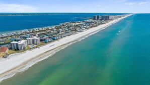 An aerial view of a coastal resort area with beachfront properties, a sandy beach, and a clear blue ocean.