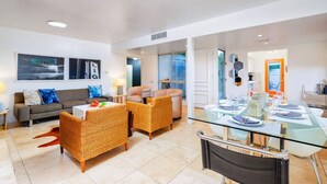 A modern living room with a sofa, two armchairs, a glass dining table set for four, and a kitchen area visible through an open door. - Perfect 4 Families, Amazing Reviews Pool & Jacuzzi (Palm Springs)