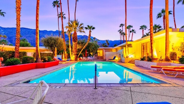 A swimming pool with lounge chairs and palm trees, surrounded by a building with a view of mountains. - Perfect 4 Families, Amazing Reviews Pool & Jacuzzi (Palm Springs)