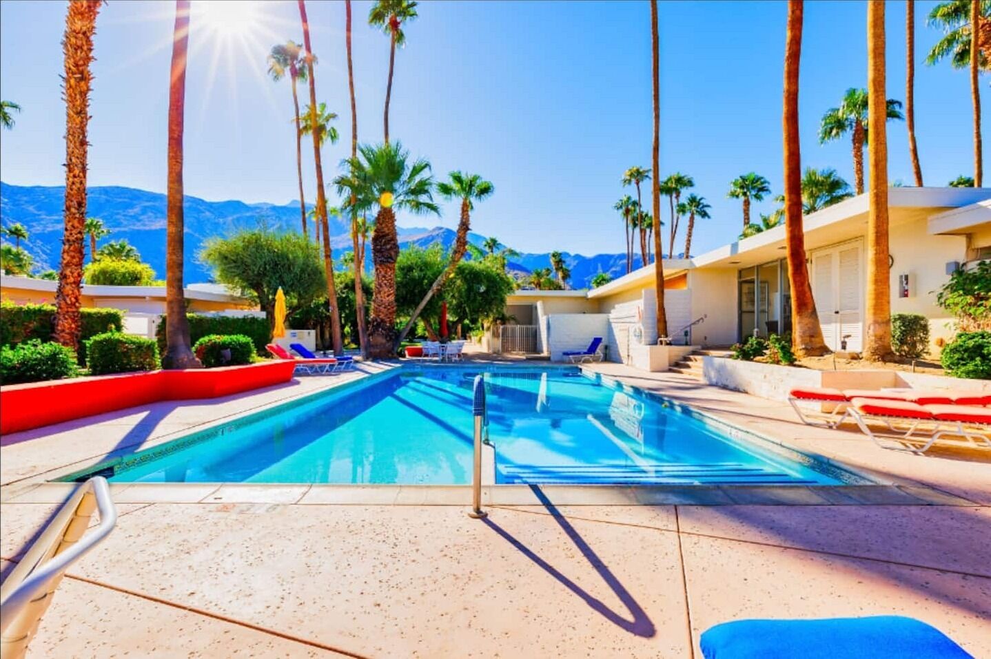 A swimming pool with lounge chairs, palm trees, and a mountain view.