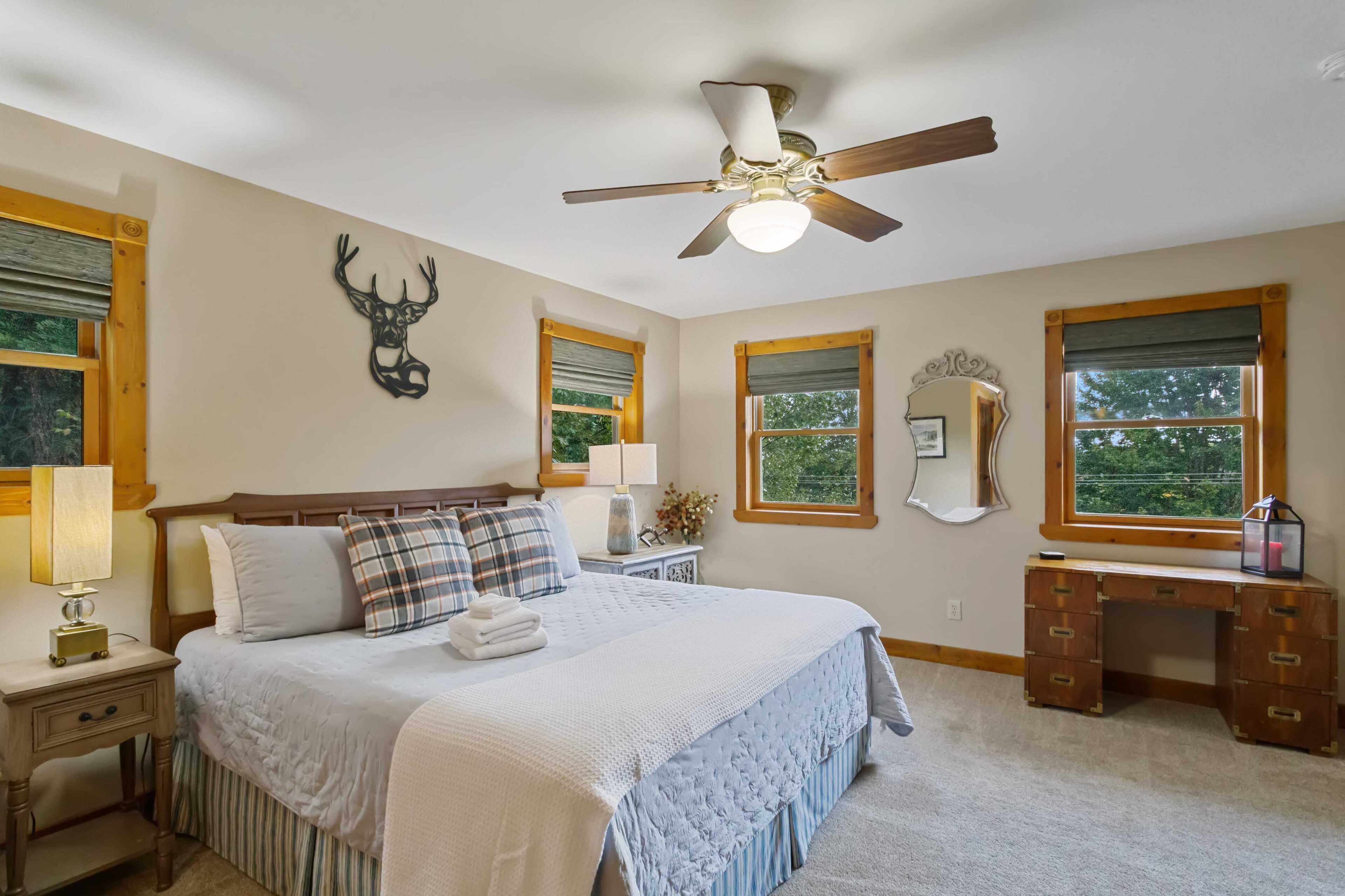 Une chambre à coucher comprenant un lit, des tables de chevet, un bureau, un ventilateur de plafond et une décoration murale représentant une tête de cerf.