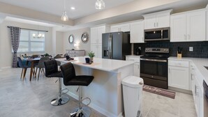 Una cocina moderna con armarios blancos, un refrigerador negro, electrodomésticos de acero inoxidable y una zona de bar con taburetes.