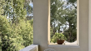 A balcony with a white table and chairs, a potted plant, and a view of trees. - Villa Monacelli (Fano)