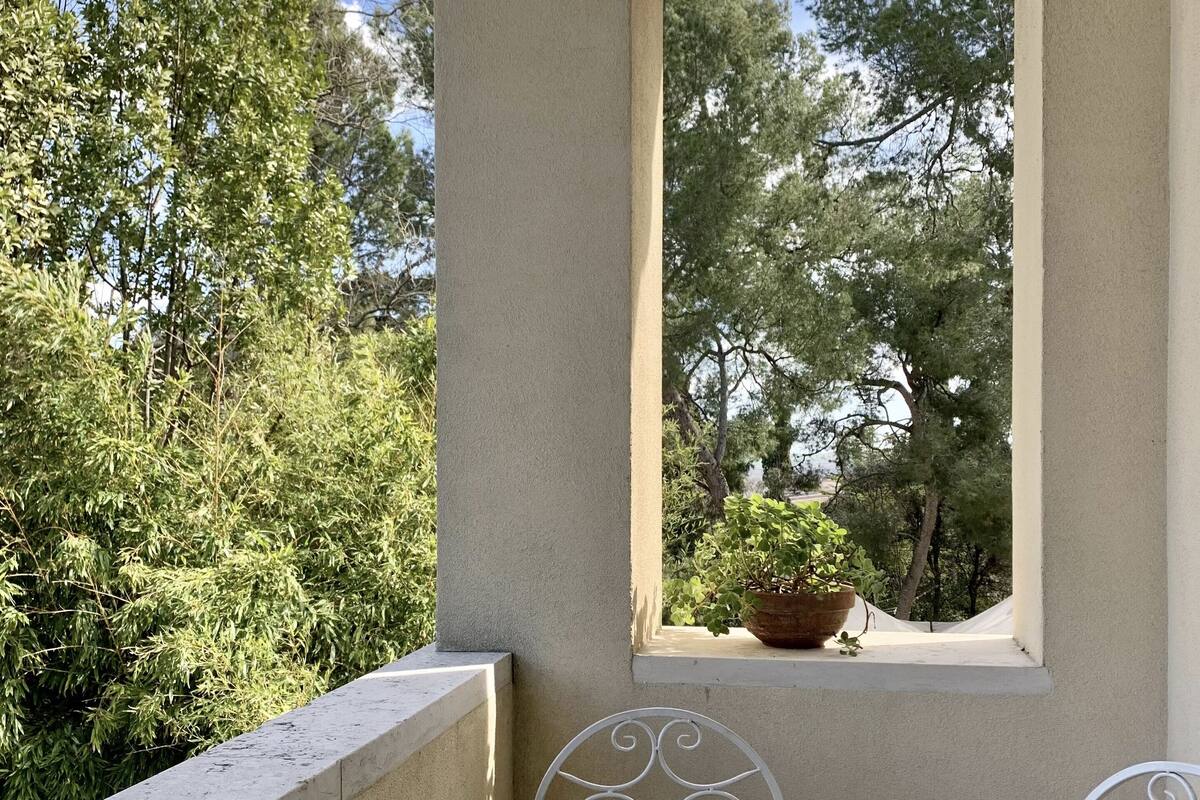 A balcony with a white table and chairs, a potted plant, and a view of trees.