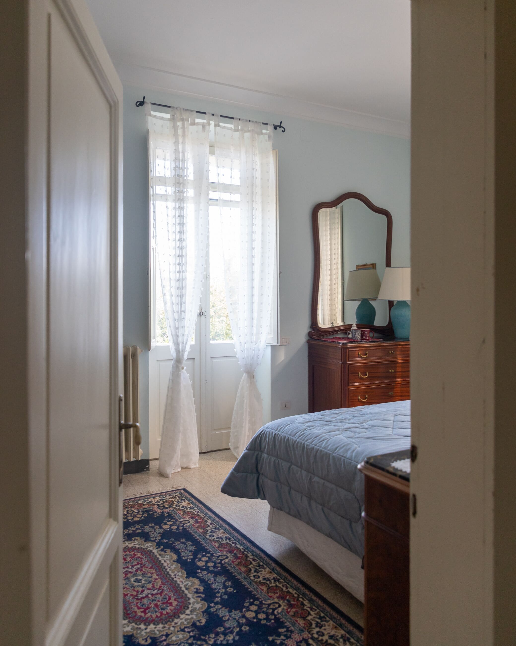 A bedroom with a bed, a dresser, a mirror, and a window with curtains.