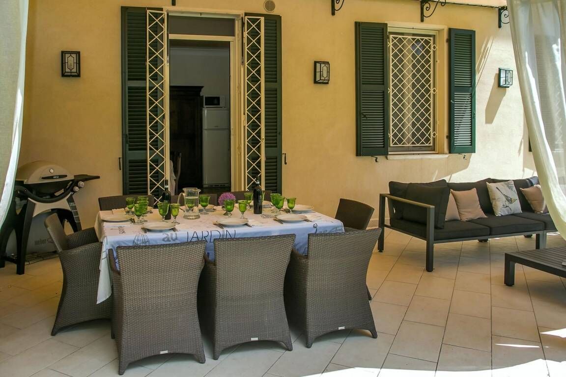 Un coin repas avec une table dressée pour quatre personnes, entouré de chaises en osier, d’un canapé et d’un barbecue.