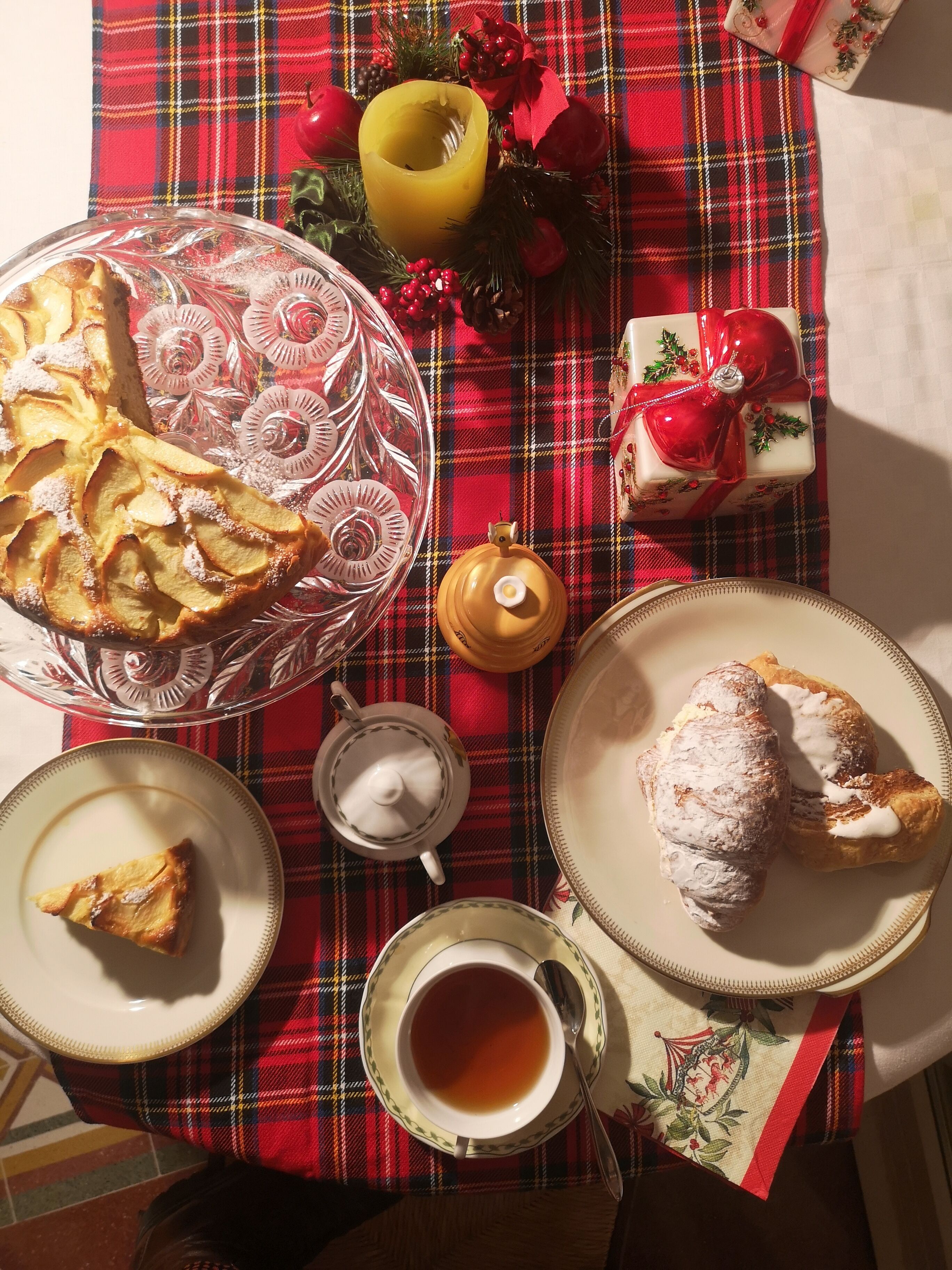 A table set with a variety of food items, including a pie, pastries, and a cup of tea, on a plaid tablecloth.