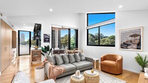 Ein modernes Wohnzimmer mit grauem Sofa, einem braunen Sessel und einem Essbereich mit Tisch und Stühlen.